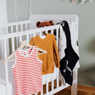 A warm baby room with a crib, clothes, and playful decorations.